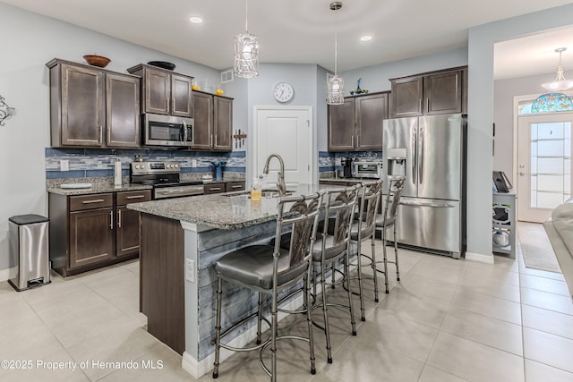 kitchen featuring pendant lighting, sink, appliances with stainless steel finishes, a kitchen breakfast bar, and an island with sink