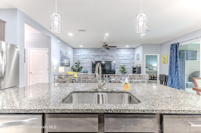 kitchen with a kitchen island with sink, sink, light stone counters, and stainless steel appliances