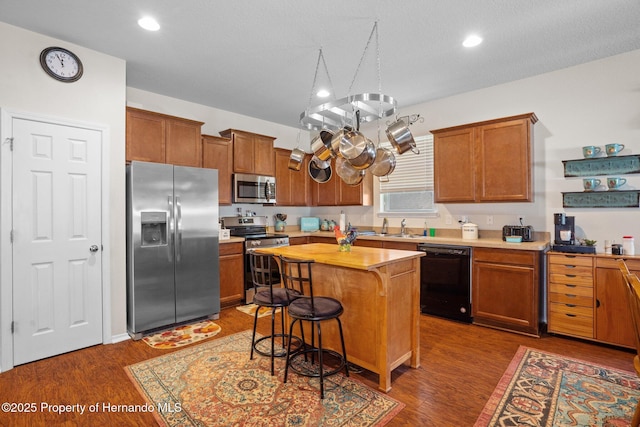 kitchen with dark hardwood / wood-style flooring, a kitchen island, a breakfast bar area, and appliances with stainless steel finishes