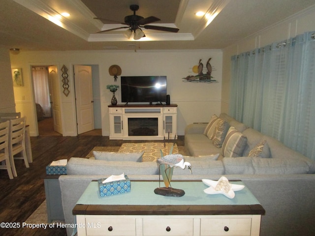 living room with ceiling fan, crown molding, dark wood-type flooring, and a tray ceiling