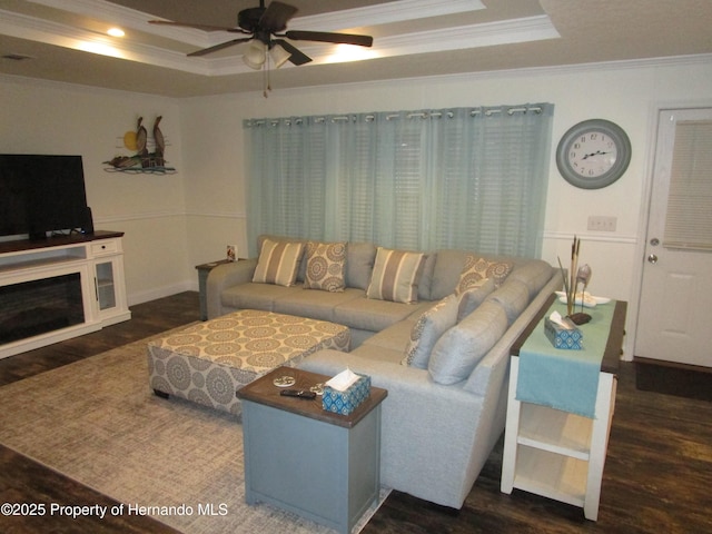 living room with crown molding, dark wood-type flooring, ceiling fan, and a tray ceiling