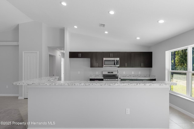 kitchen with light tile patterned floors, vaulted ceiling, a kitchen island with sink, and appliances with stainless steel finishes