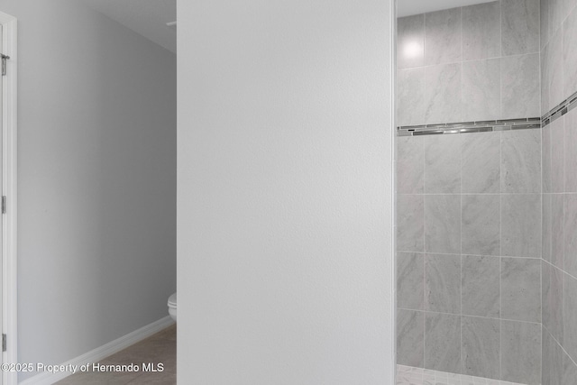 bathroom featuring tile patterned floors, toilet, and a tile shower