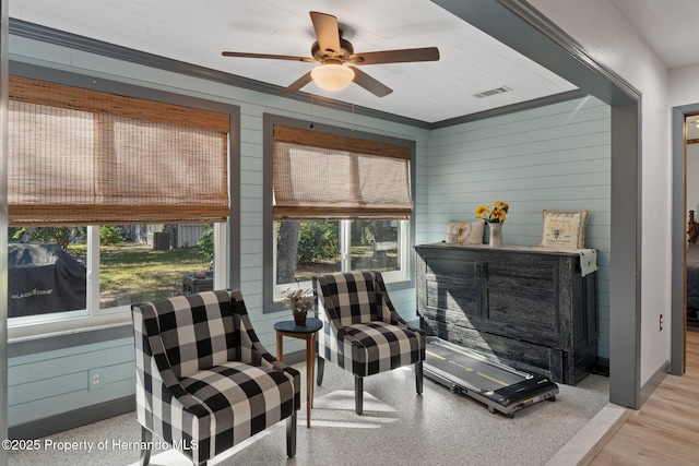 living area featuring ceiling fan, ornamental molding, and wooden walls