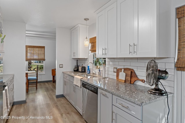 kitchen featuring tasteful backsplash, decorative light fixtures, light wood-type flooring, dishwasher, and white cabinets