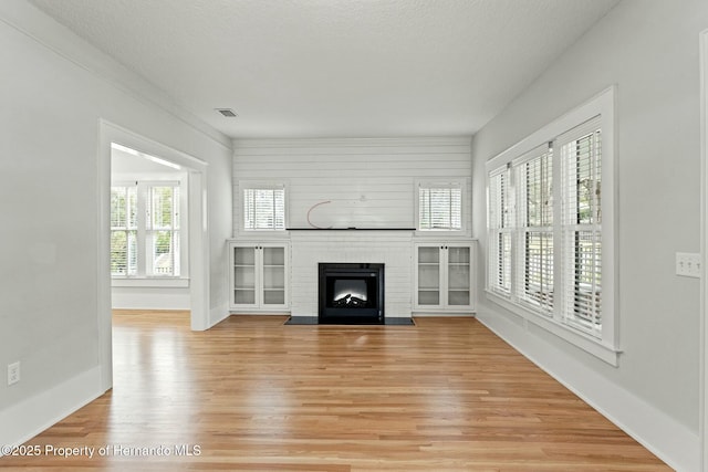 unfurnished living room featuring a healthy amount of sunlight, hardwood / wood-style floors, a textured ceiling, and a fireplace