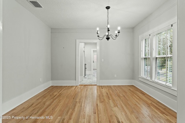 spare room featuring wood-type flooring, a textured ceiling, and a notable chandelier