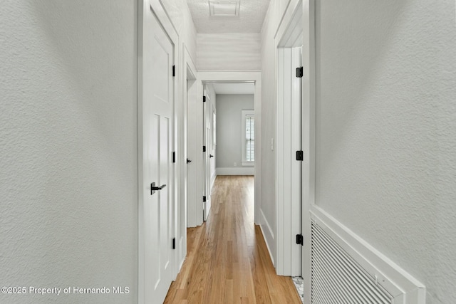 hallway featuring light hardwood / wood-style floors and a textured ceiling