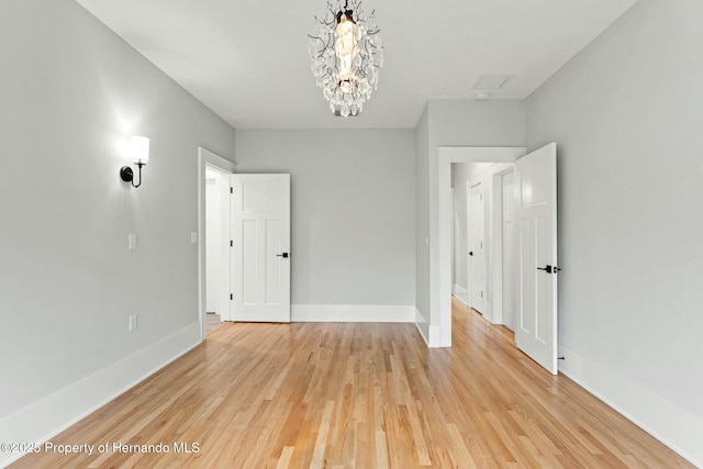 empty room with a notable chandelier and light hardwood / wood-style flooring