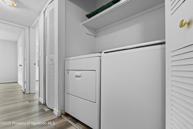 laundry room featuring washer and clothes dryer, a textured ceiling, and light hardwood / wood-style flooring