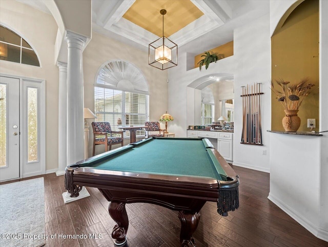 recreation room featuring ornate columns, a high ceiling, dark wood-type flooring, and a tray ceiling