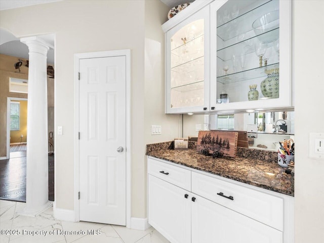 bar featuring dark stone countertops, decorative columns, and white cabinets