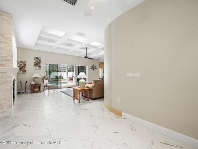 living room featuring coffered ceiling, a stone fireplace, a skylight, ceiling fan, and beam ceiling