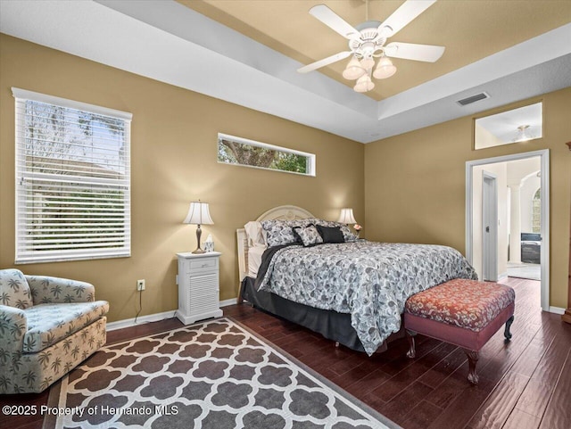 bedroom with dark hardwood / wood-style flooring, ceiling fan, and a tray ceiling