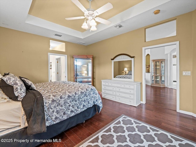 bedroom featuring a raised ceiling, dark hardwood / wood-style flooring, ceiling fan, and ornate columns