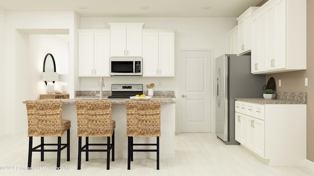 kitchen featuring white cabinetry, appliances with stainless steel finishes, light stone countertops, and a breakfast bar area