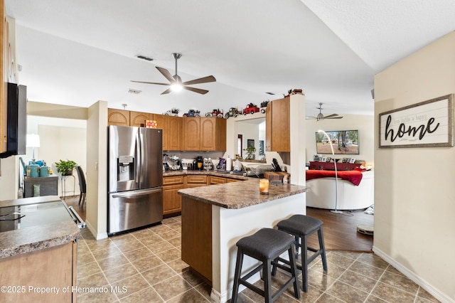 kitchen with vaulted ceiling, stainless steel fridge with ice dispenser, a kitchen breakfast bar, ceiling fan, and kitchen peninsula