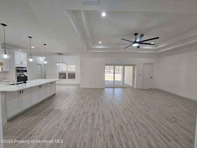 unfurnished living room featuring sink, light hardwood / wood-style flooring, ceiling fan, and a tray ceiling