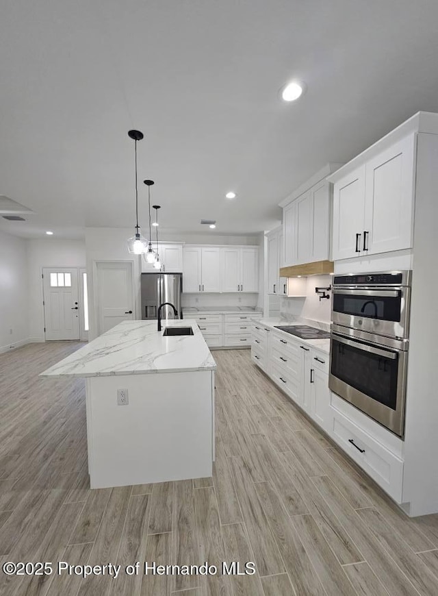 kitchen featuring sink, appliances with stainless steel finishes, white cabinets, a center island with sink, and decorative light fixtures