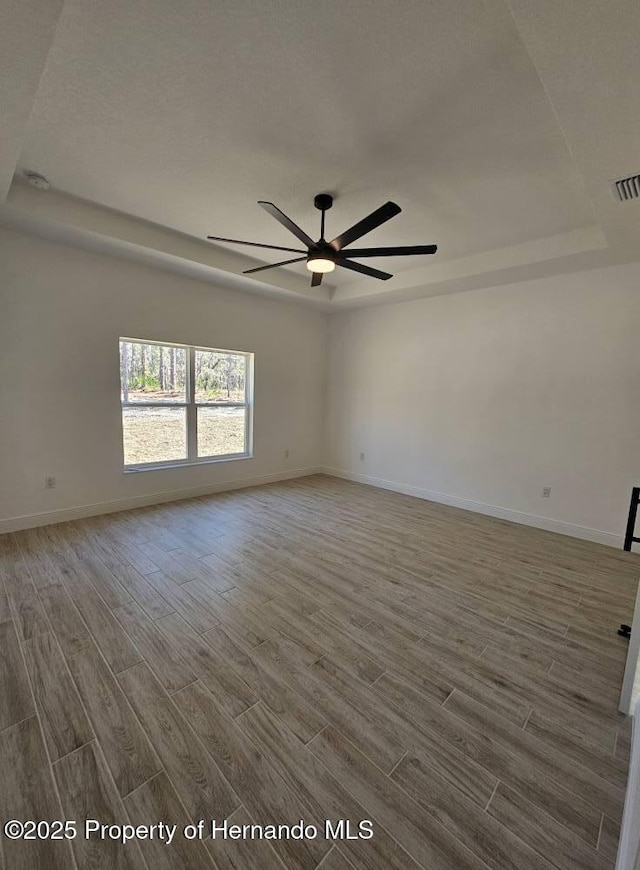 unfurnished room with ceiling fan, wood-type flooring, and a tray ceiling