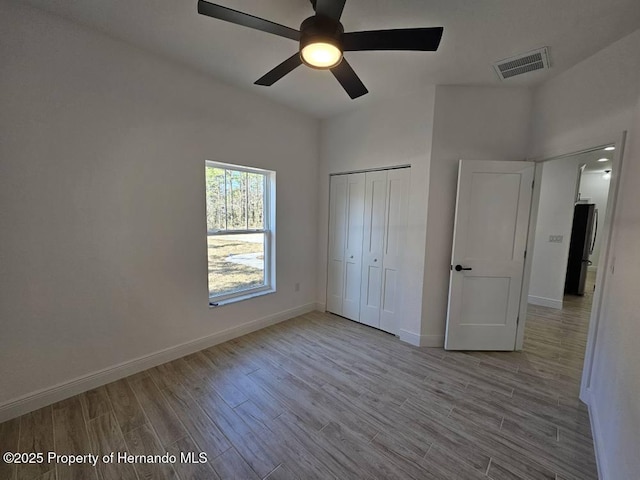 unfurnished bedroom with ceiling fan, stainless steel fridge, light hardwood / wood-style floors, and a closet