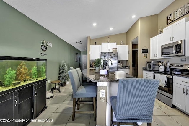 kitchen with light tile patterned floors, appliances with stainless steel finishes, a kitchen breakfast bar, white cabinets, and a kitchen island