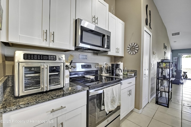 kitchen with lofted ceiling, stainless steel appliances, dark stone countertops, and white cabinets