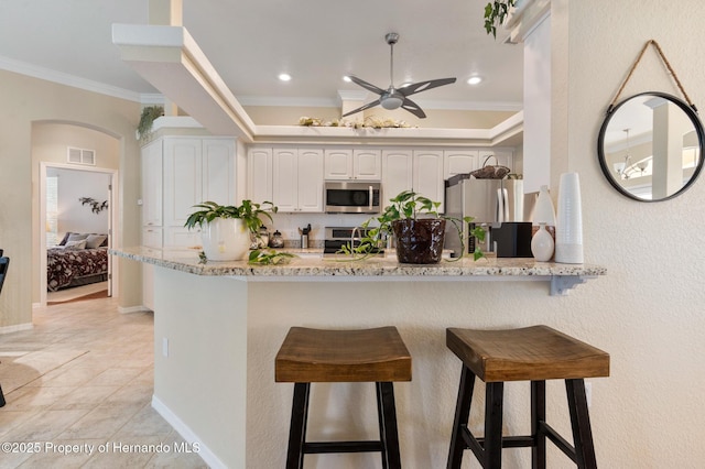 kitchen with ornamental molding, appliances with stainless steel finishes, white cabinets, and a kitchen bar