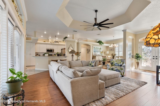 living room with a raised ceiling, ornamental molding, ceiling fan with notable chandelier, and light hardwood / wood-style floors