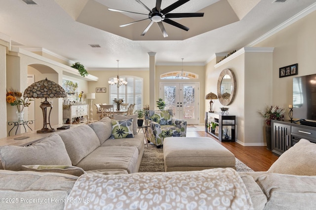 living room featuring french doors, crown molding, wood-type flooring, a tray ceiling, and ceiling fan with notable chandelier