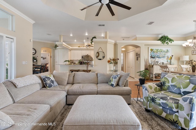 living room with crown molding, a healthy amount of sunlight, ceiling fan with notable chandelier, and light hardwood / wood-style flooring