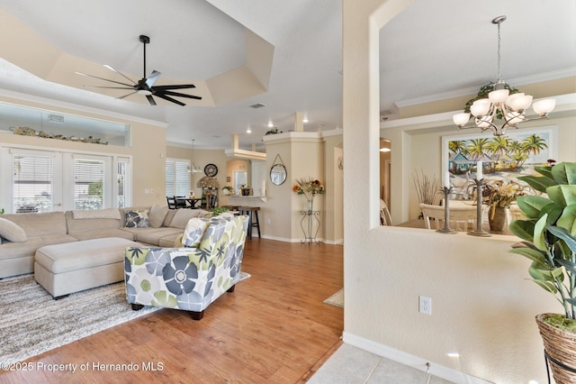 living room with crown molding, light hardwood / wood-style flooring, a tray ceiling, ceiling fan with notable chandelier, and french doors