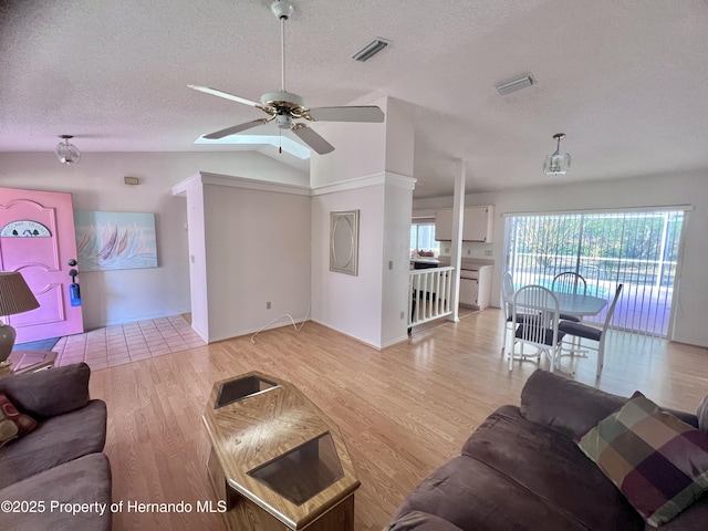 living room with ceiling fan, light hardwood / wood-style flooring, a textured ceiling, and vaulted ceiling