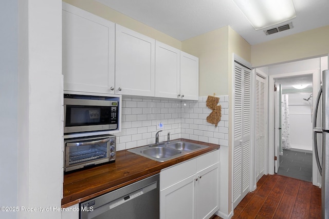 kitchen featuring butcher block counters, sink, white cabinetry, appliances with stainless steel finishes, and backsplash