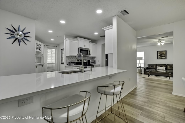 kitchen with a breakfast bar area, white cabinetry, light hardwood / wood-style floors, a textured ceiling, and kitchen peninsula