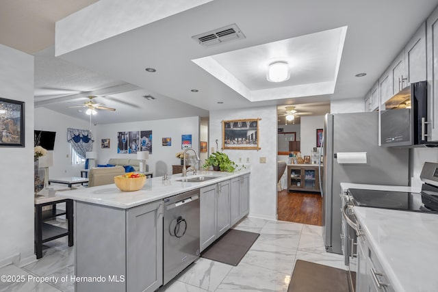 kitchen with sink, appliances with stainless steel finishes, gray cabinets, a raised ceiling, and ceiling fan