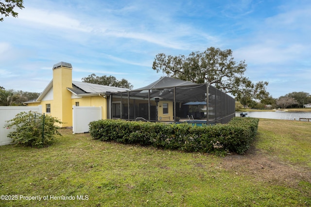 rear view of property with a water view, a lawn, and solar panels