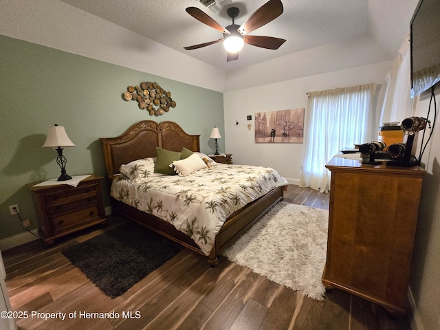 bedroom with dark hardwood / wood-style flooring, a tray ceiling, and ceiling fan