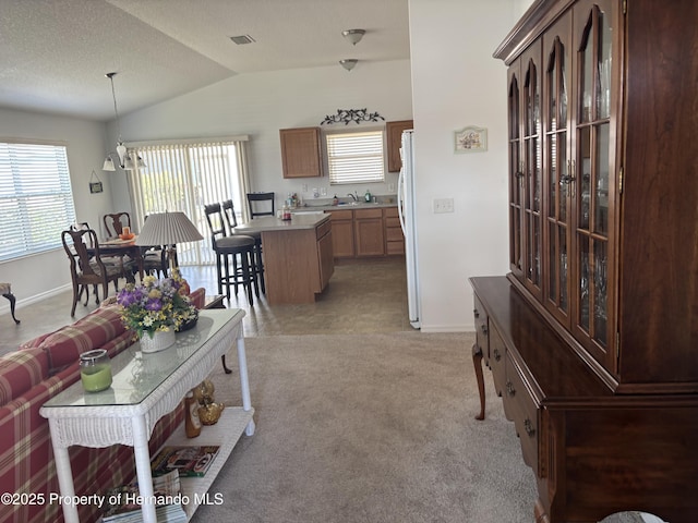 living area with light carpet, lofted ceiling, visible vents, and baseboards