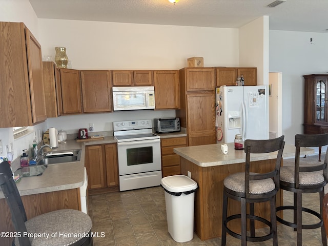 kitchen featuring brown cabinets, a breakfast bar area, light countertops, a sink, and white appliances