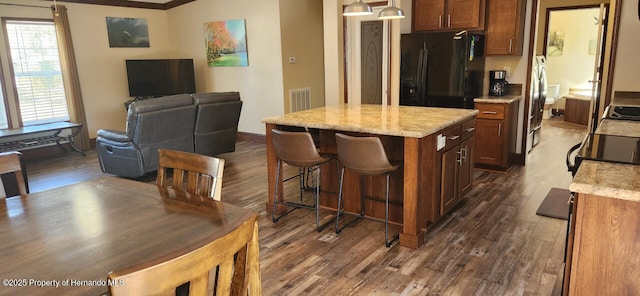 kitchen featuring black fridge, crown molding, decorative light fixtures, a center island, and dark hardwood / wood-style flooring