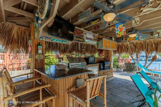 view of patio / terrace with grilling area, a ceiling fan, exterior kitchen, a bar, and fence