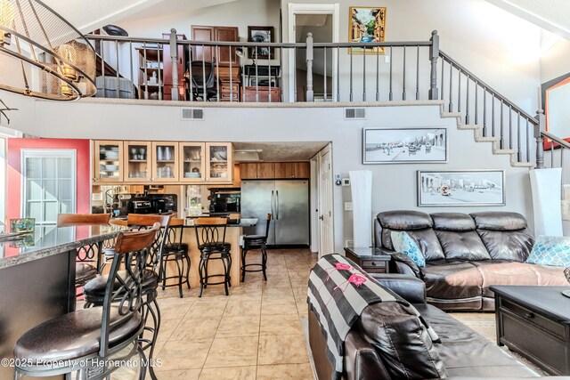 living area with stairs, light tile patterned flooring, visible vents, and a towering ceiling