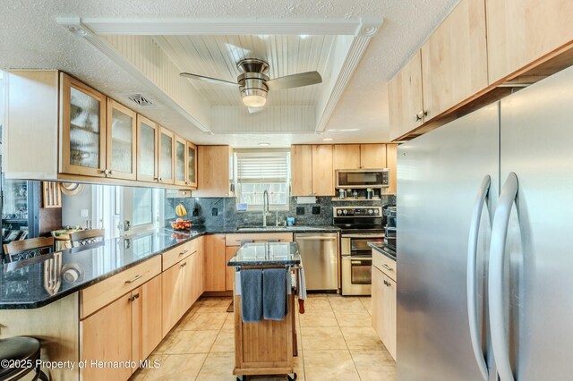 kitchen featuring light brown cabinets, dark stone counters, a sink, appliances with stainless steel finishes, and backsplash