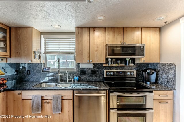 kitchen featuring a textured ceiling, appliances with stainless steel finishes, decorative backsplash, and a sink