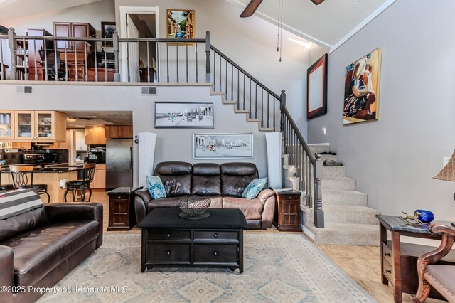 living room featuring stairway, high vaulted ceiling, ceiling fan, and visible vents