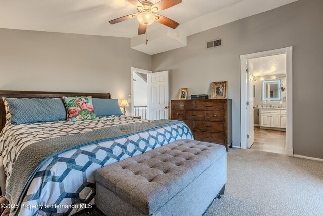 bedroom featuring ceiling fan, light colored carpet, visible vents, baseboards, and ensuite bath