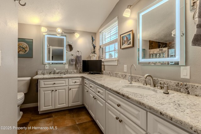 full bath with a tile shower, a sink, double vanity, toilet, and lofted ceiling