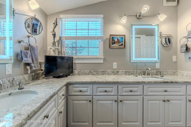 full bath with a sink, vaulted ceiling, and double vanity