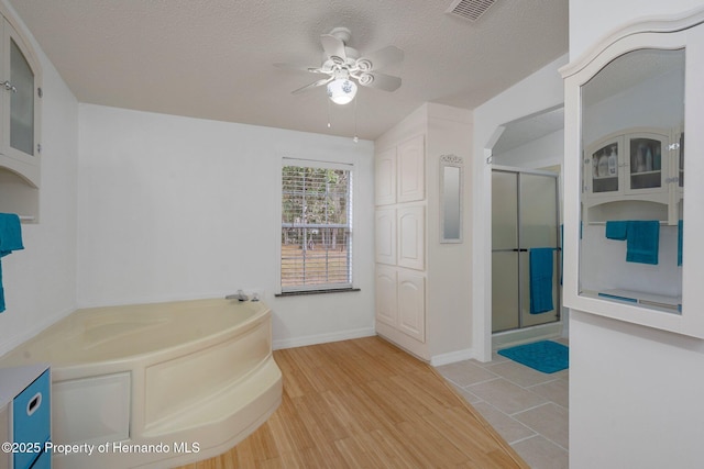 bathroom featuring ceiling fan, hardwood / wood-style flooring, plus walk in shower, and a textured ceiling